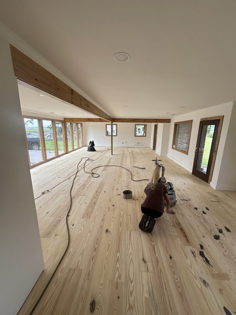 Person sanding wooden floor in large room.